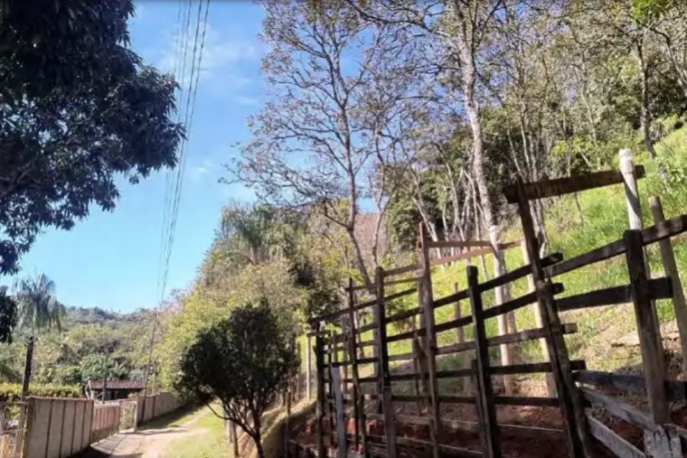 Porteira de madeira e cerca, com morros ao fundo.