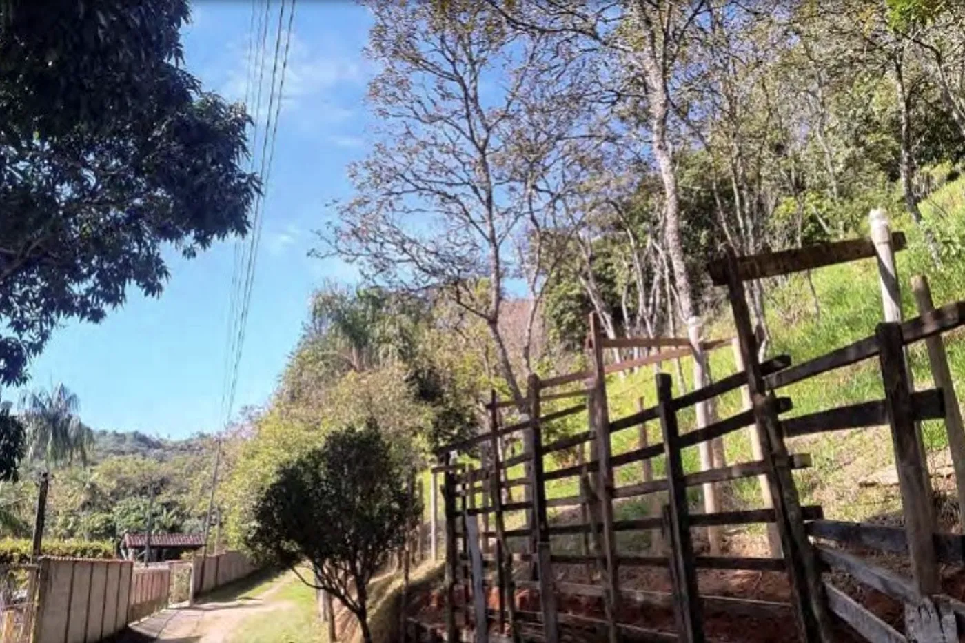 Cerca de divisa em porteira de madeira, com relevo de morros ao fundo.
