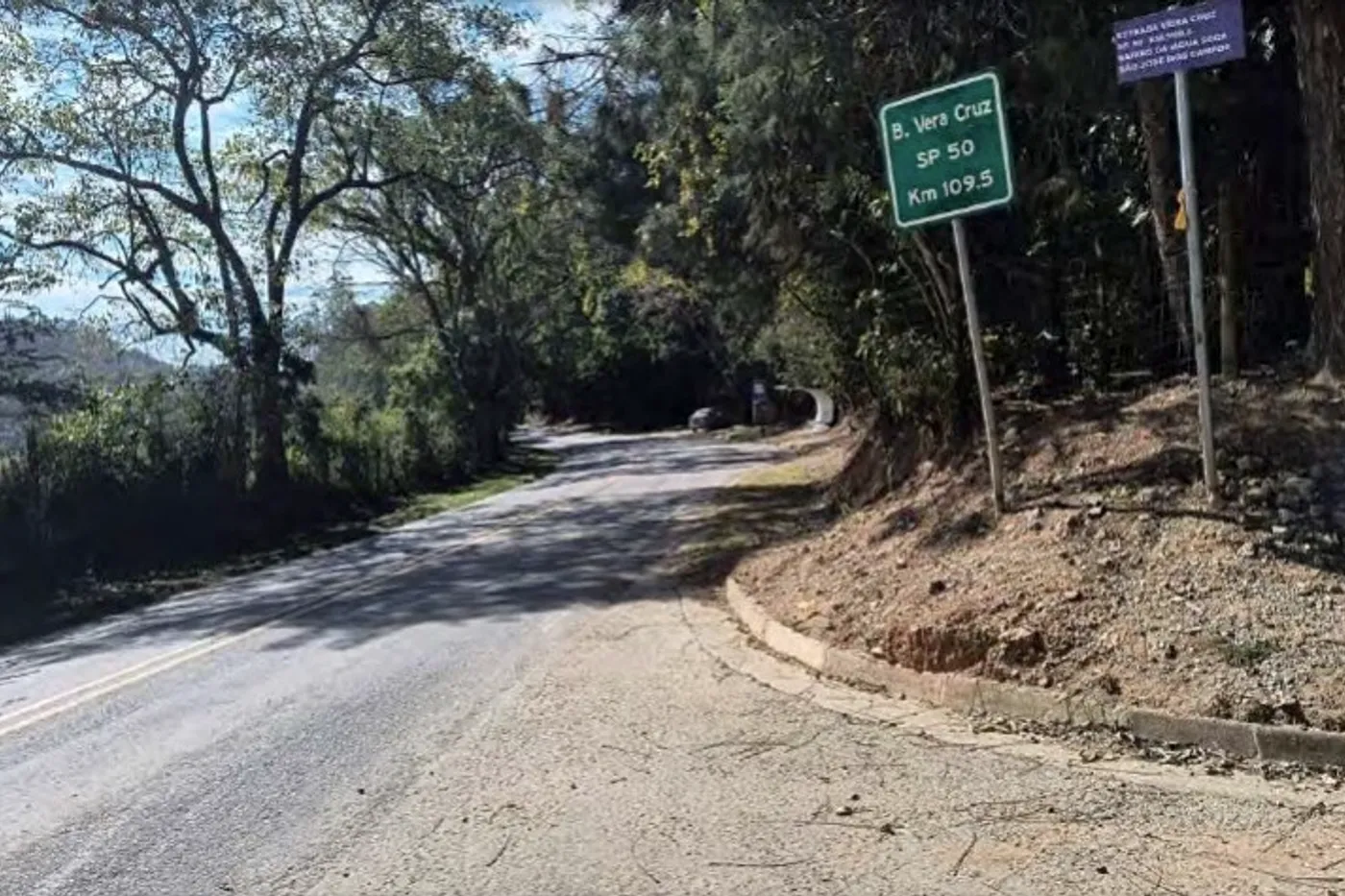 Estrada rural asfaltada com placa de identificação da via, no acesso à região.